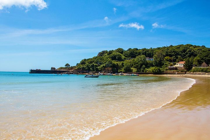 St Brelade's Bay beach, Jersey — calm turquoise water and a wooded headland